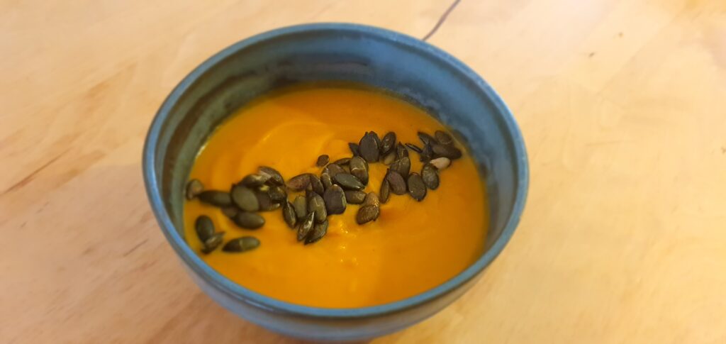 Photo d'un bol bleu avec une soupe orange à l'intérieur et une ligne de graines de courges au centre.